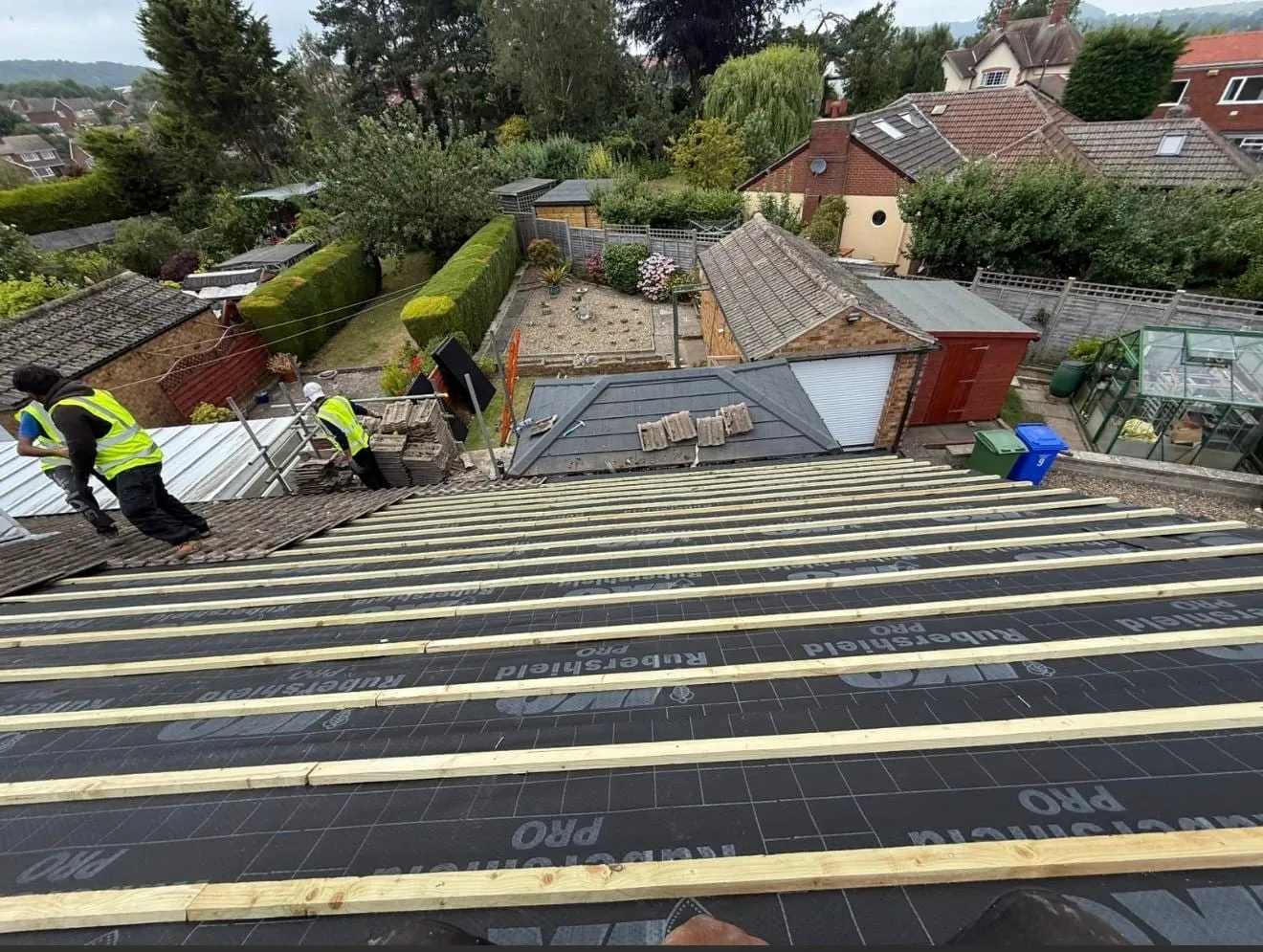 Battens fixed over black membrane on a large roof, with roofers working at the eaves