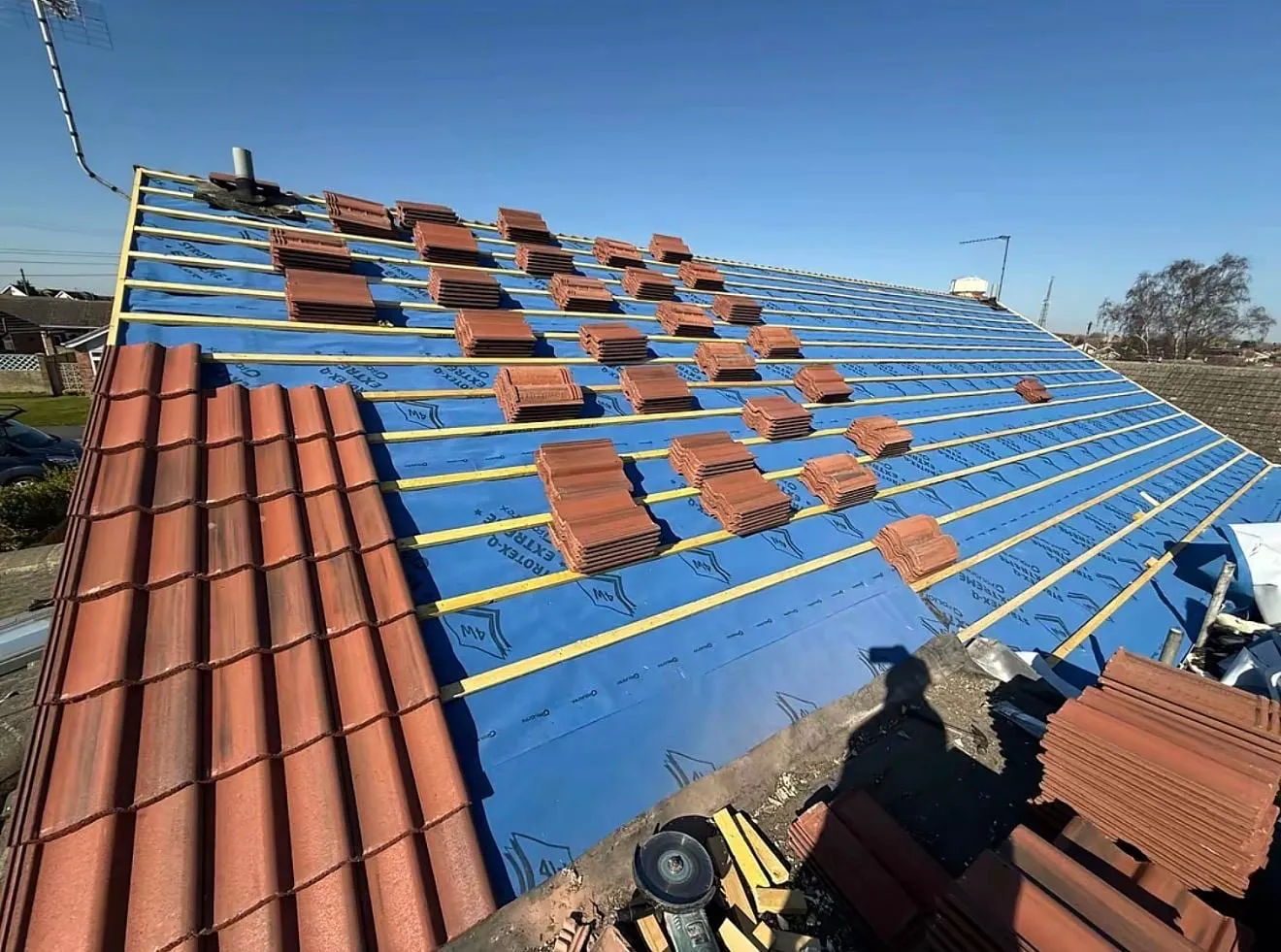 Blue breathable membrane and battens with stacks of red tiles ready to lay
