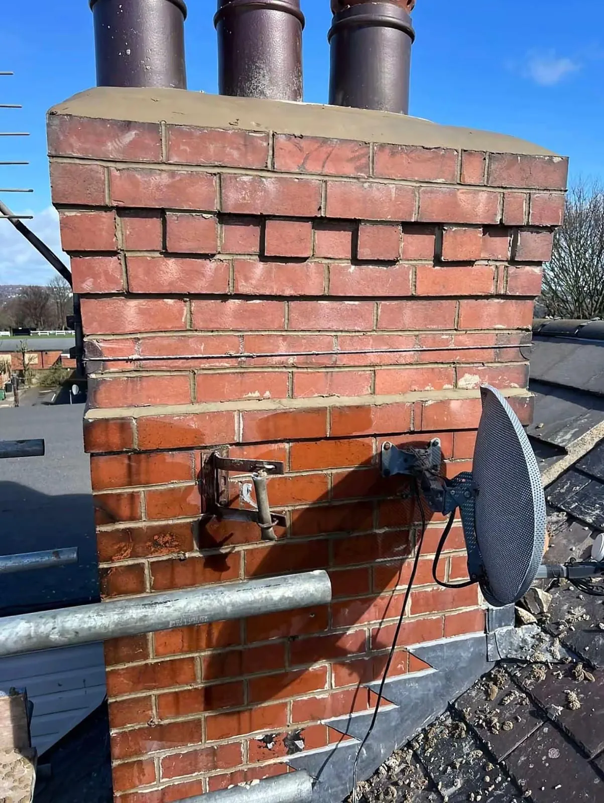 Brick chimney stack with fresh pointing and three pots, with a satellite dish