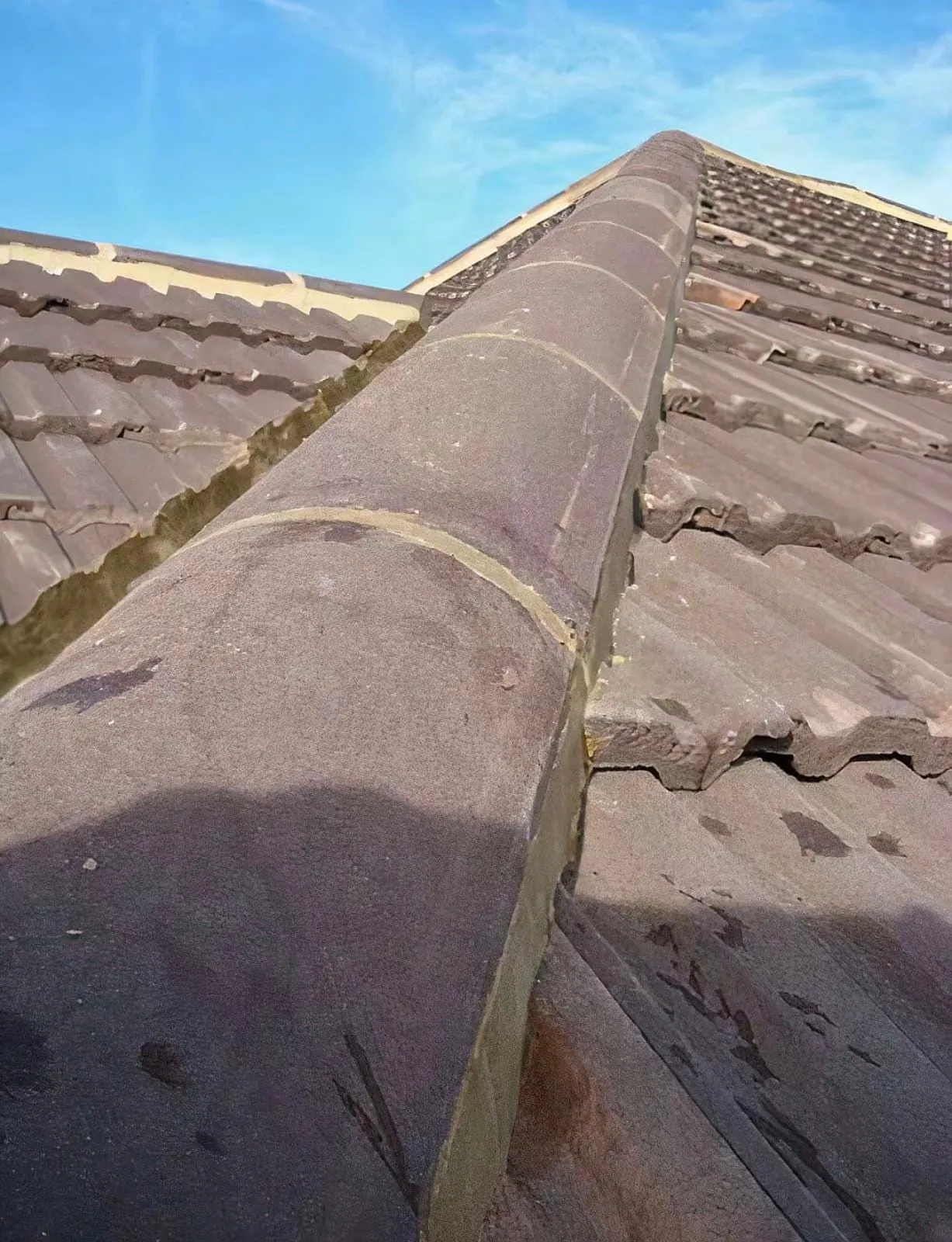 Close-up of weathered ridge tiles with cracked mortar bedding