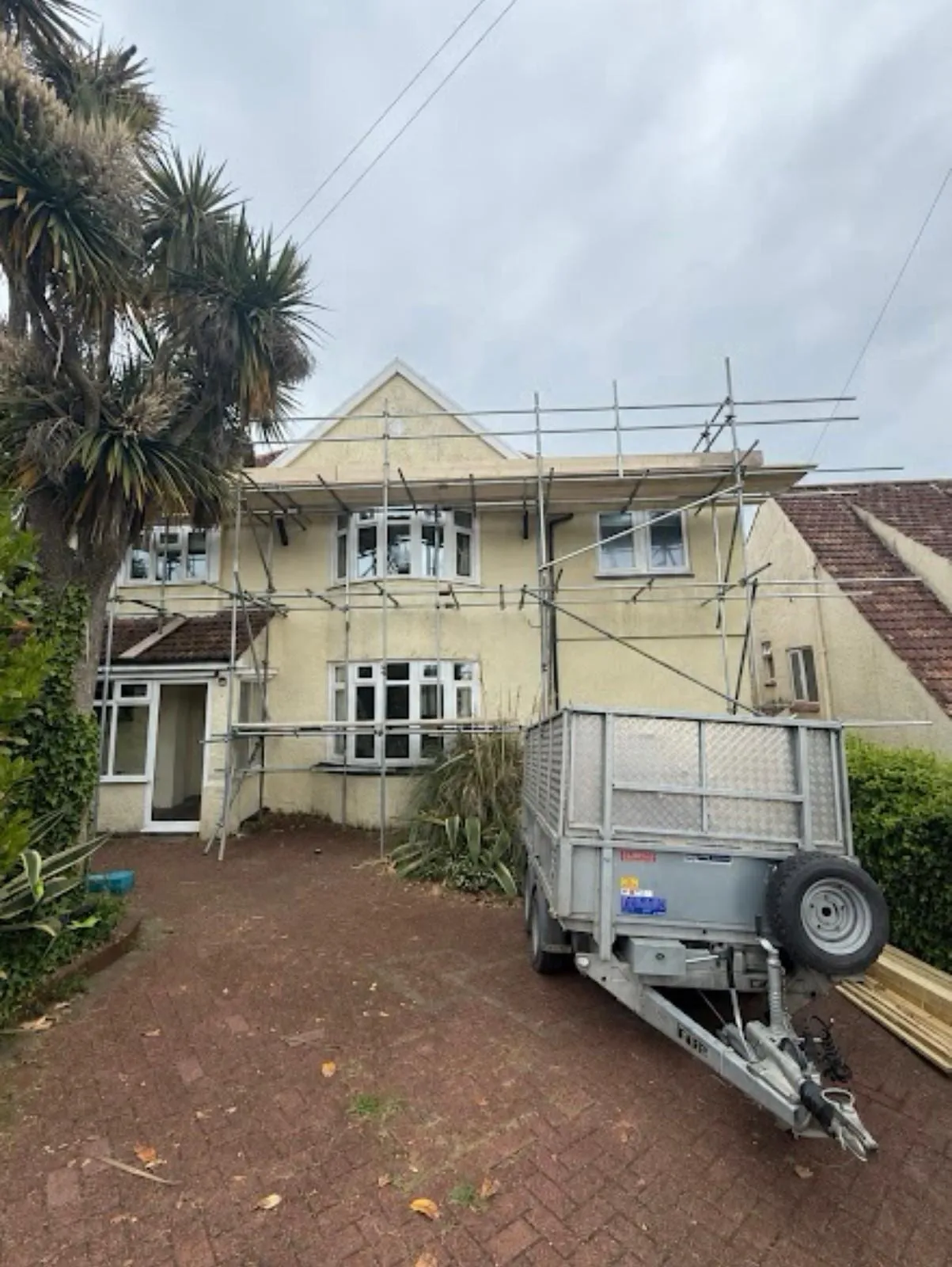 Cream-rendered house with scaffold up and a trailer on the drive
