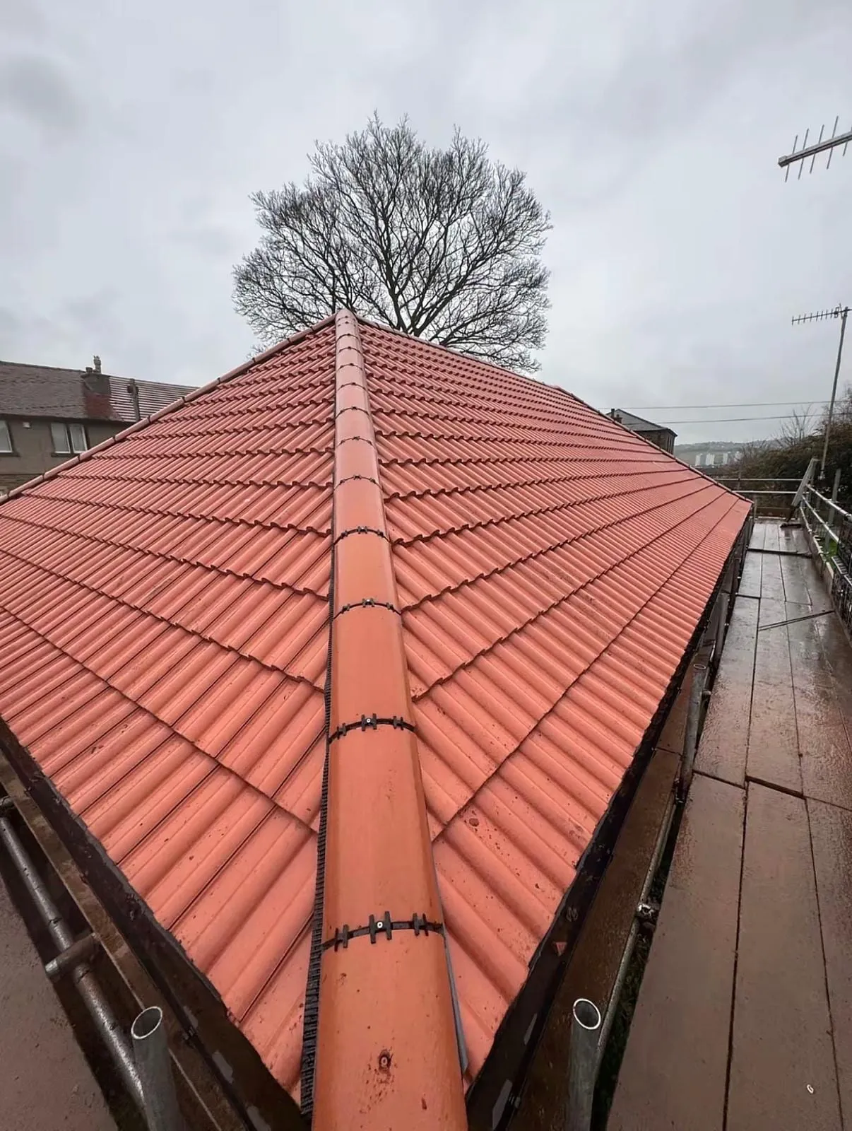 Completed red tiled hip roof with ridge tiles, seen from the scaffold