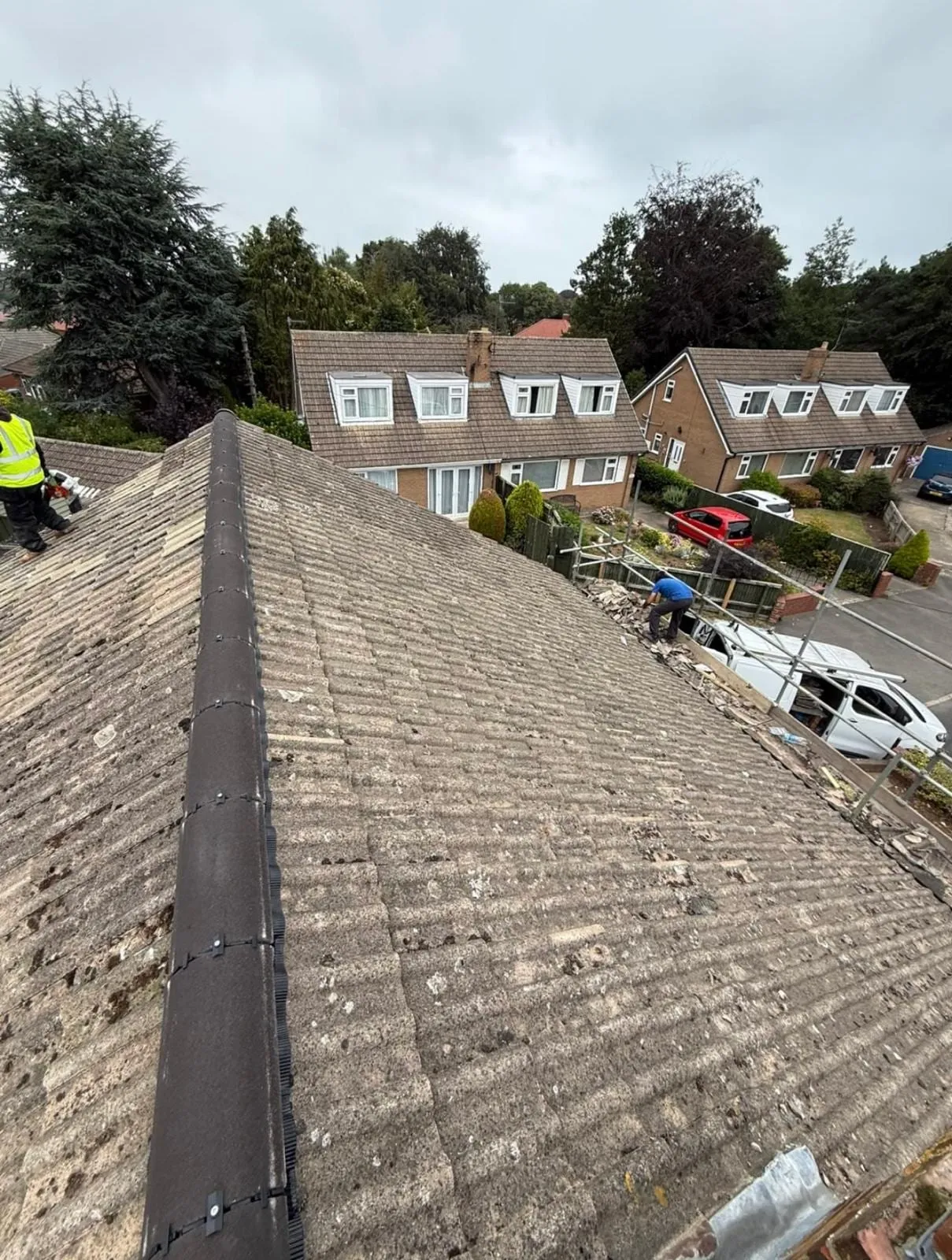 Grey roof slope running up to a ridge, with roofers working beyond it