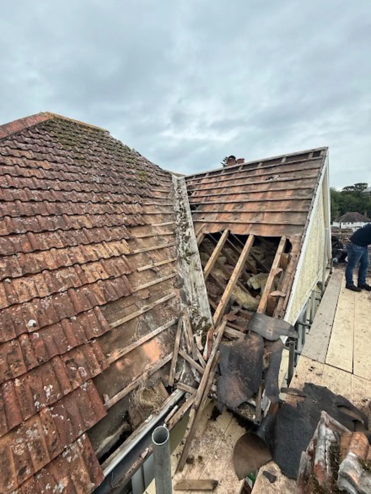 Hipped roof stripped back, with old brown tiles beside the open rafters