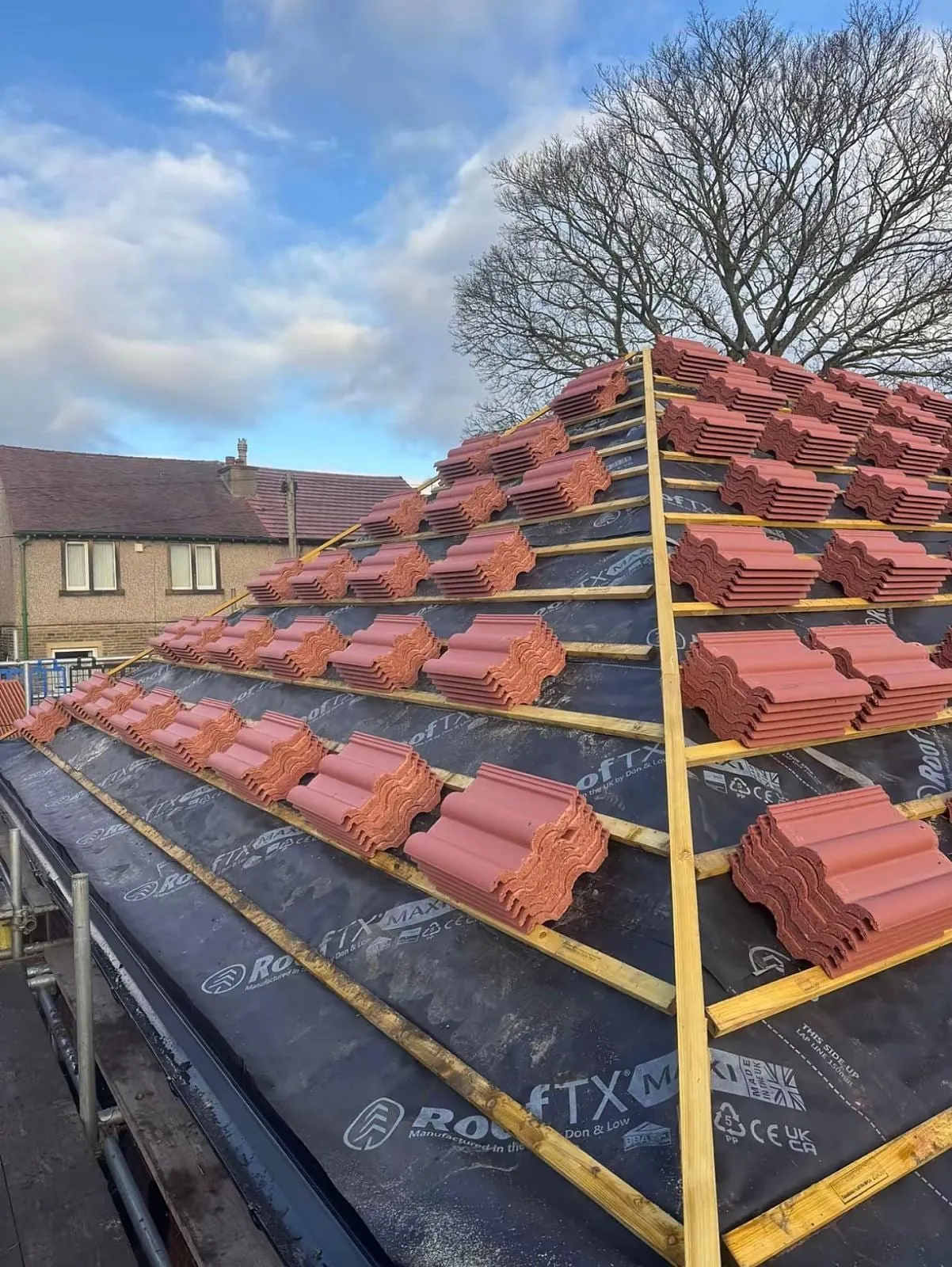 Red tiles being laid course by course over membrane and battens on a hipped roof