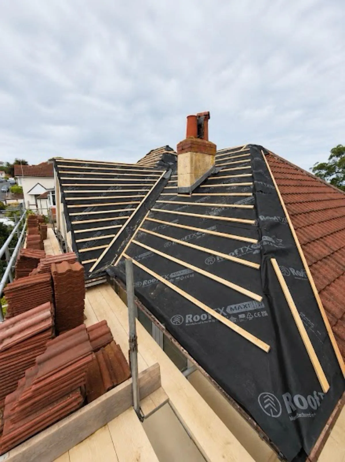 Membrane and battens on a hipped roof with a chimney and stacks of new tiles