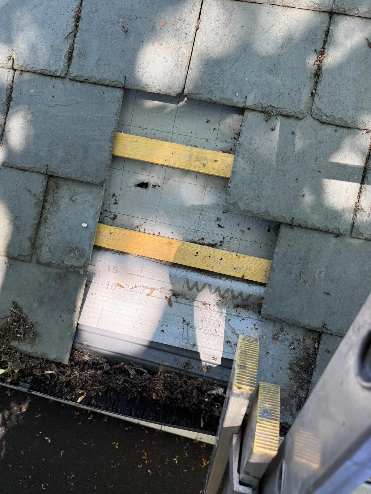 Missing slates leaving the battens exposed beside a gutter, with a repair under way