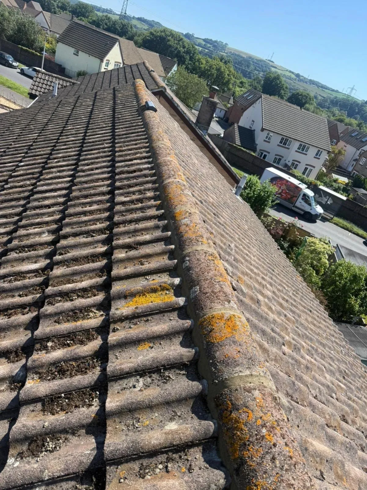 Moss-covered concrete tile roof with ridge, over a housing estate