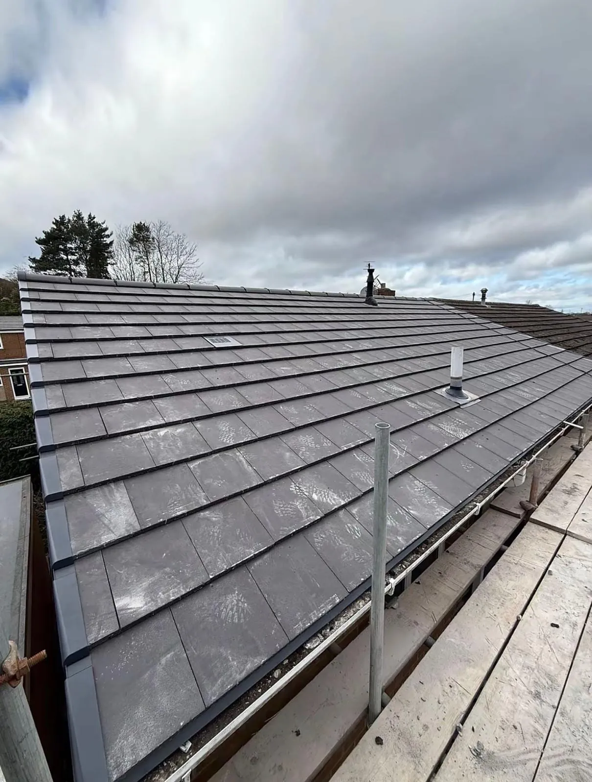 Newly laid dark flat tiles on a roof slope with scaffold edge protection