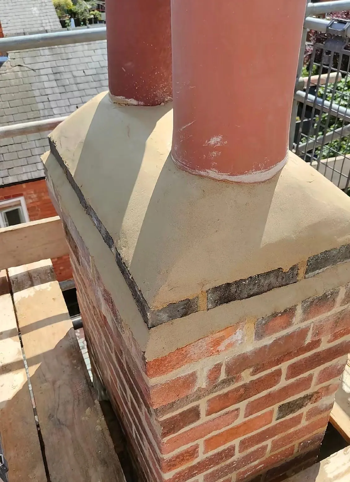 New flaunching around two terracotta chimney pots on a brick stack