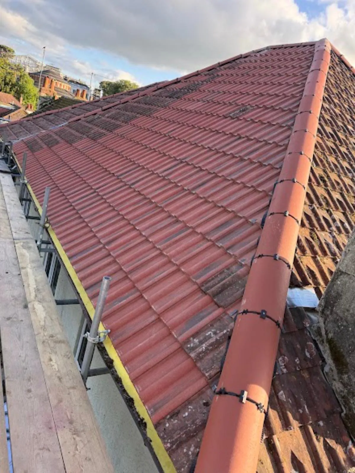 New red tiles and ridge on a hipped roof, with scaffold boards along the eaves