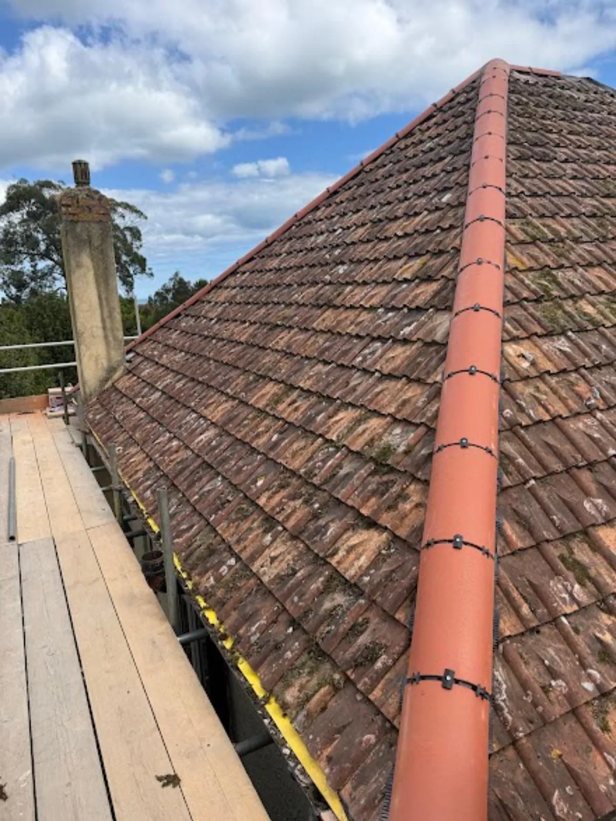 New red ridge tiles on a hipped roof beside a chimney stack
