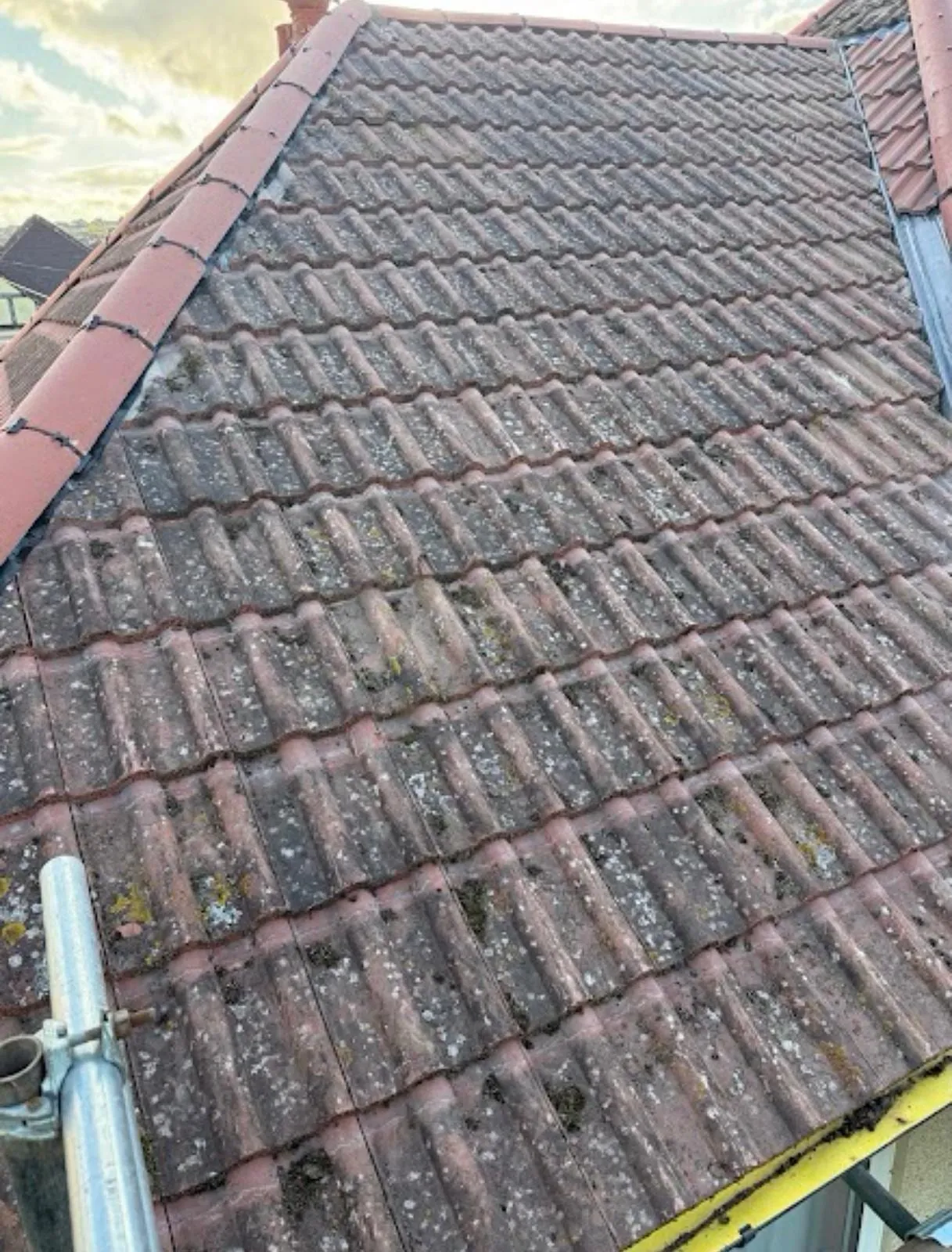 Old dark concrete tiles on a roof slope with a hip tile and scaffold