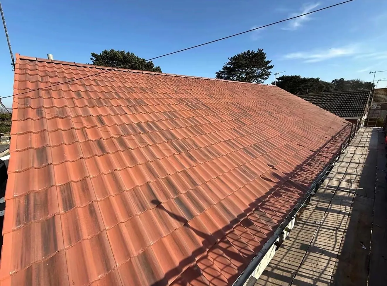 Red clay tiled roof slope with a scaffold platform along the eaves