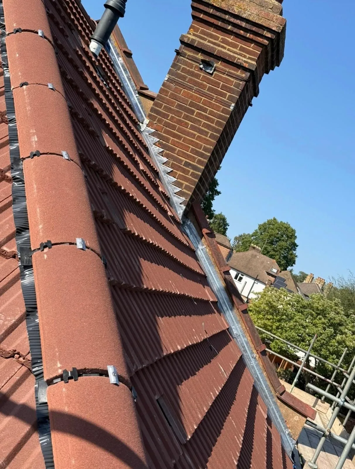 Red hip tiles beside a chimney, seen from the scaffold