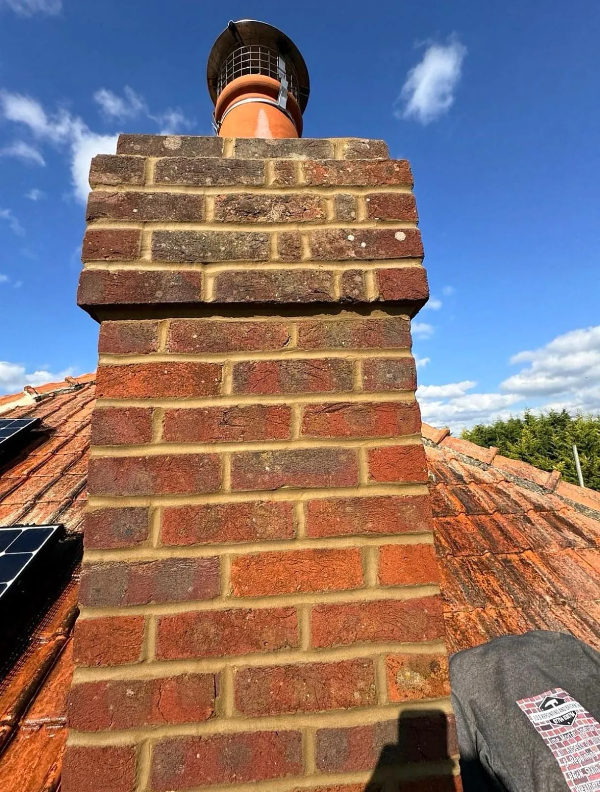 Repointed brick chimney with an orange pot against a blue sky