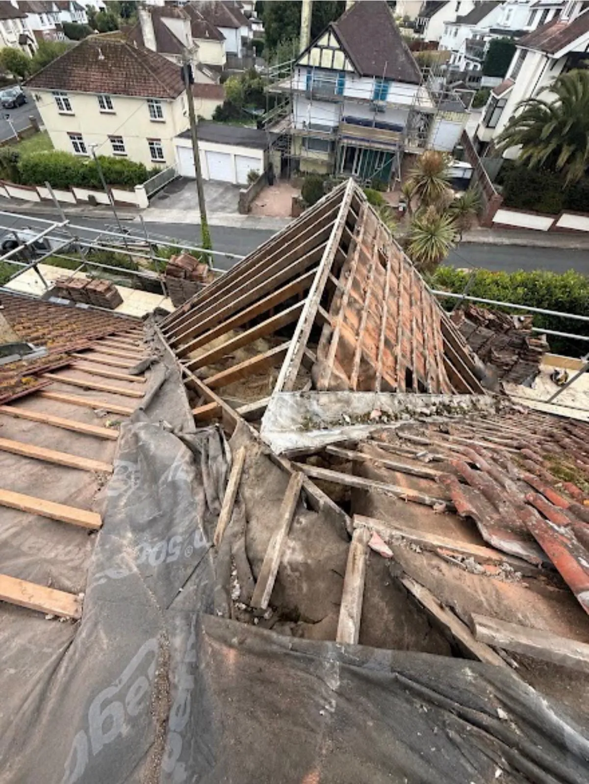 Roof structure being rebuilt, with a tarpaulin over the stripped slope