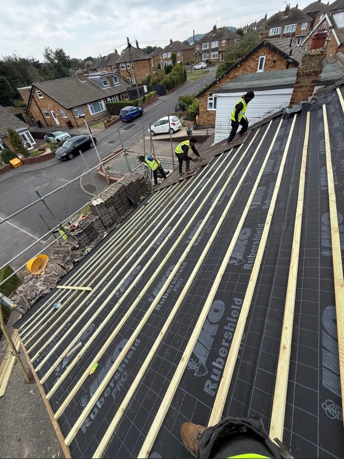 Roofers fitting battens over black membrane on a pitched roof above a residential street