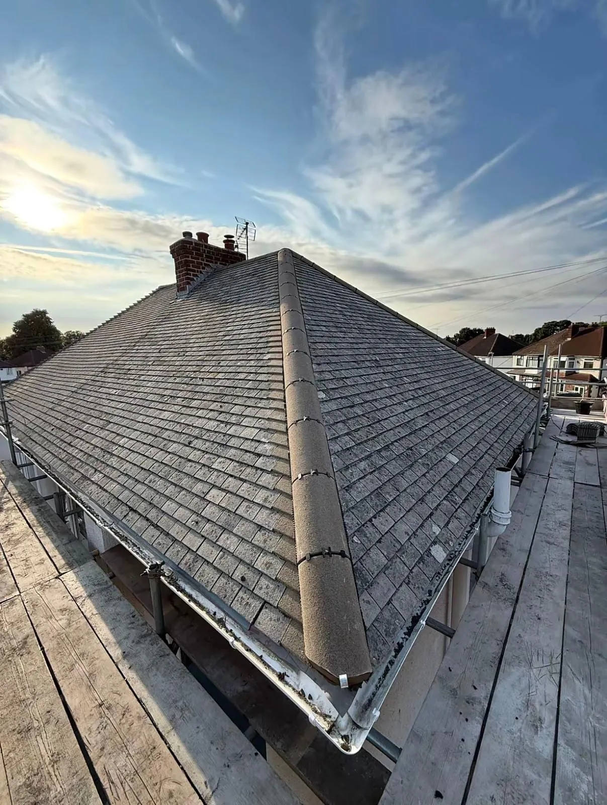 Slate hipped roof with ridge and hip tiles under a blue sky, with scaffold below