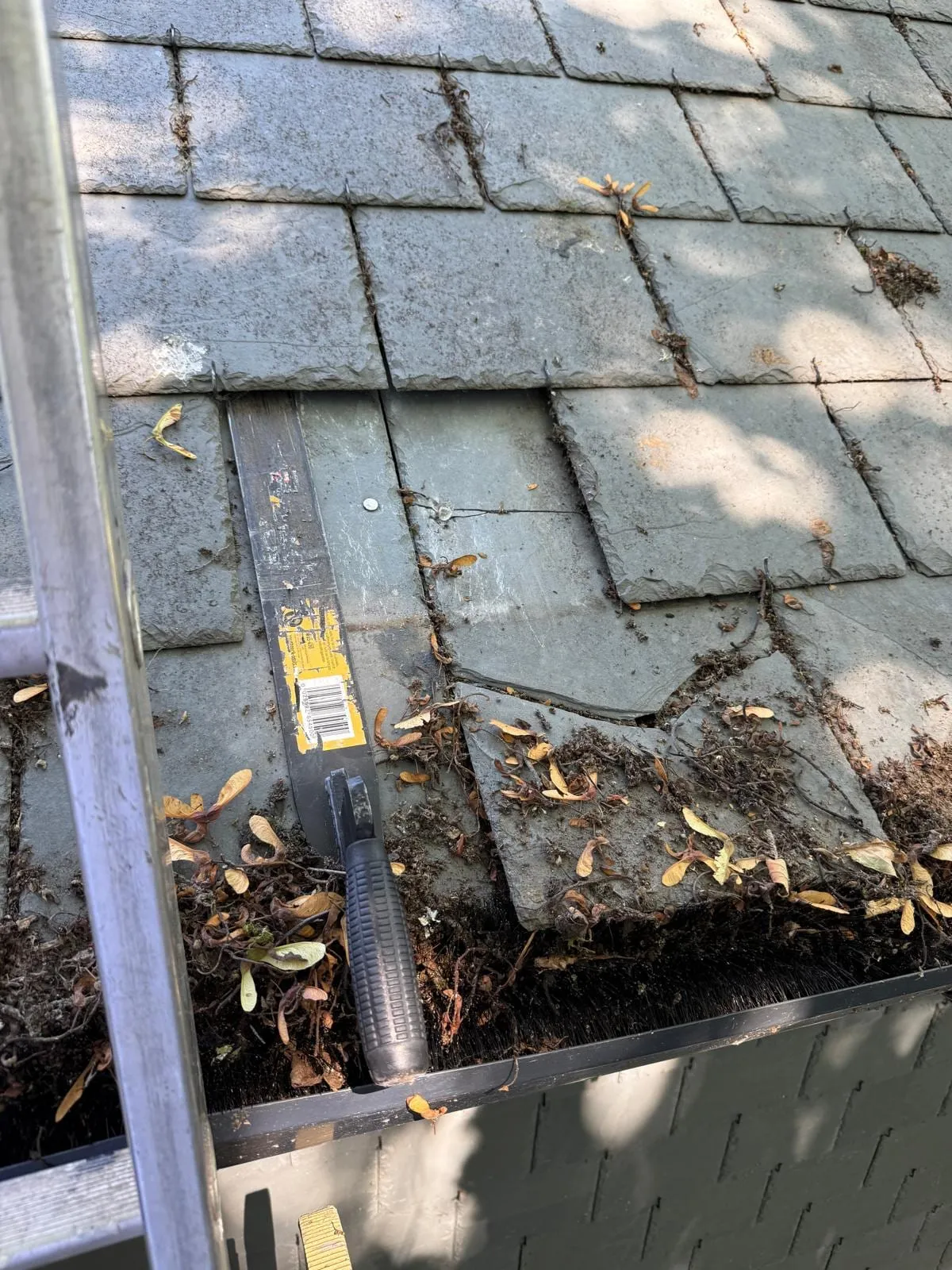 Slipped and broken slate beside a gutter full of leaves and debris