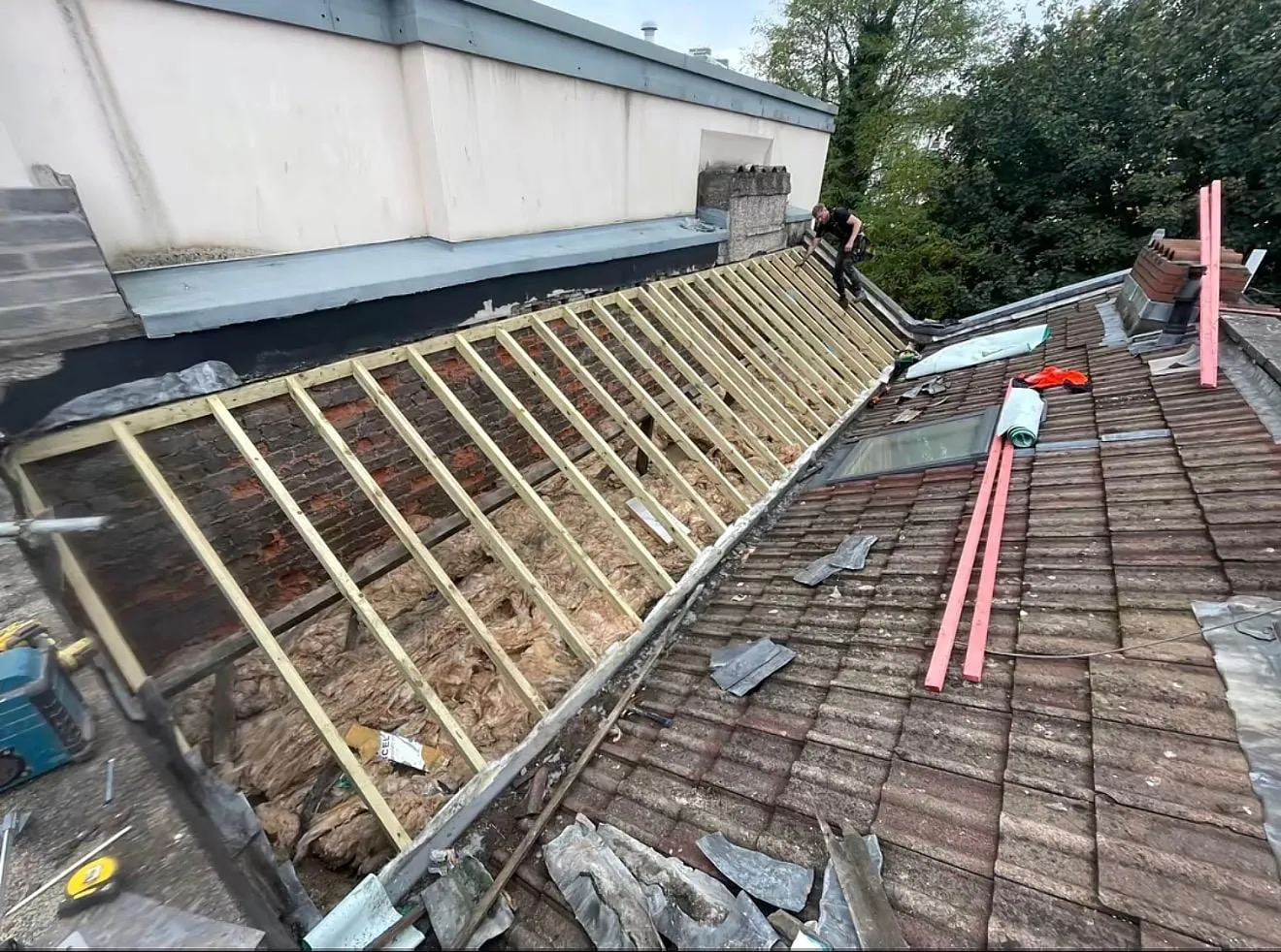 Old roof stripped back to the battens beside a parapet wall, with old tiles still on the lower slope