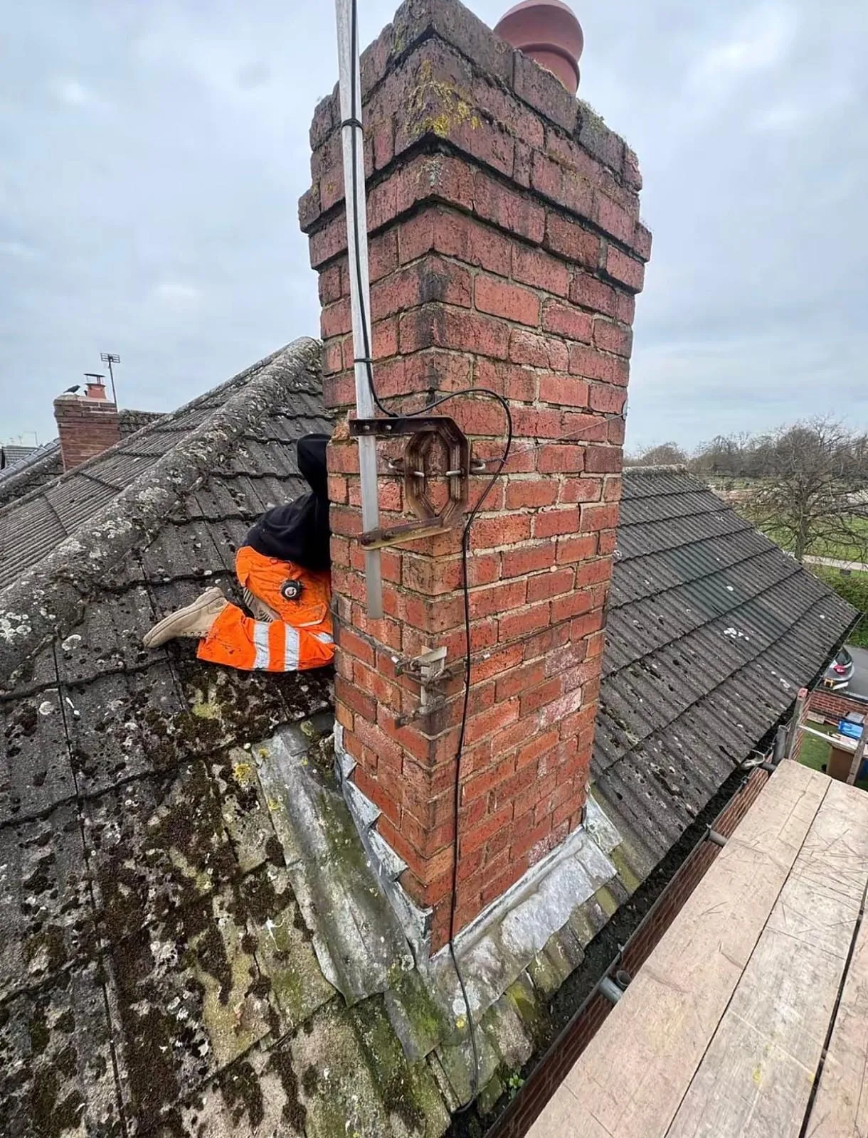 Tall brick chimney on a slate roof with a roofer at the base