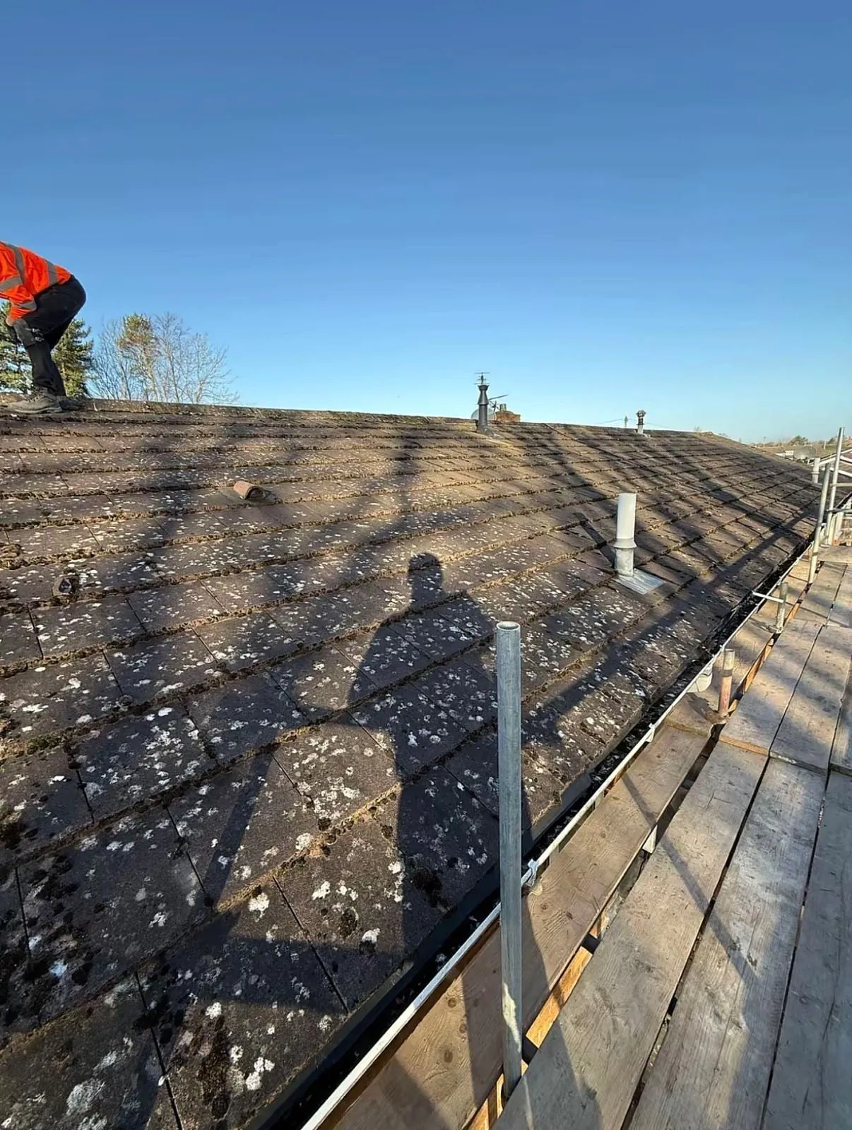 Weathered concrete tile roof with a roofer at the ridge